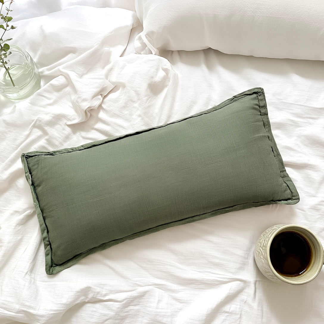 Green pillow on a white bed with a cup of coffee and a plant.