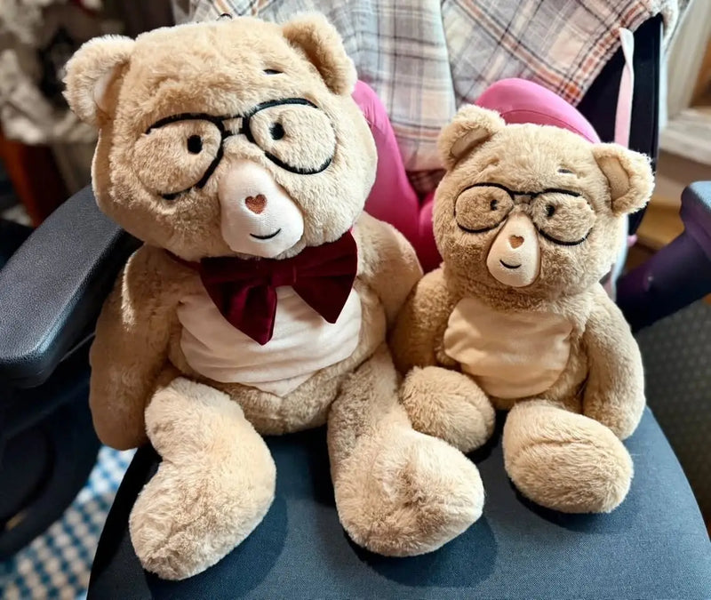 Two Percy bears wearing glasses and bow ties on a chair.