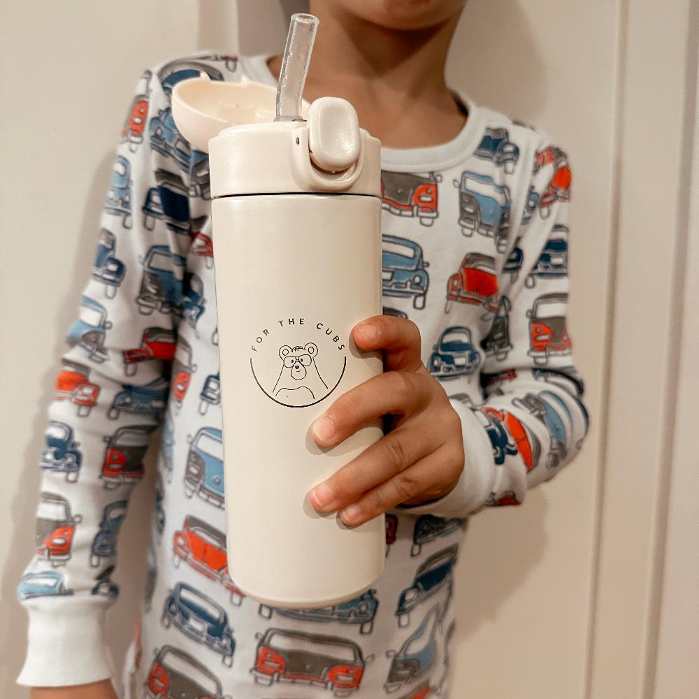 Young boy holding cream water bottle with cap off and silicone straw showing