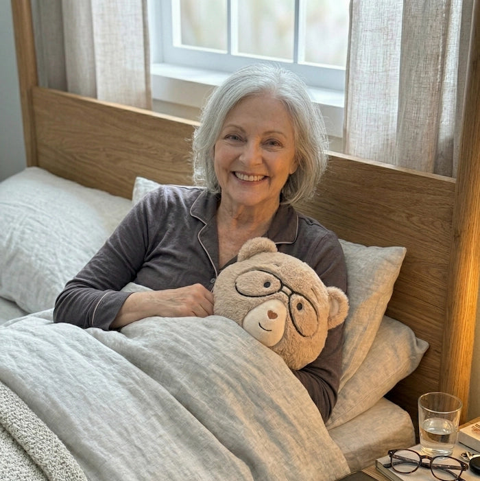Woman sitting on a bed with a Percy bear, smiling at the camera.