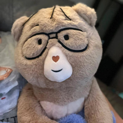 Percy bear with glasses and a heart on its nose, sitting on a blue surface.