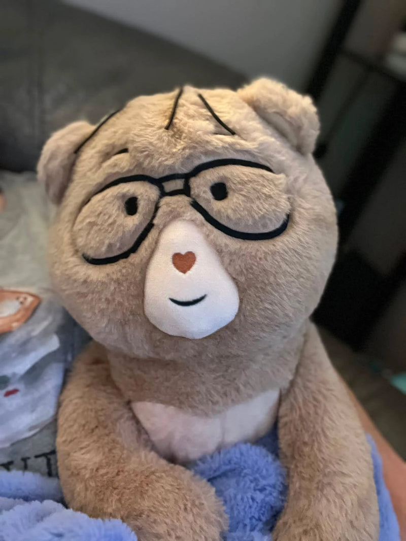 Percy bear with glasses and a heart on its nose, sitting on a blue surface.