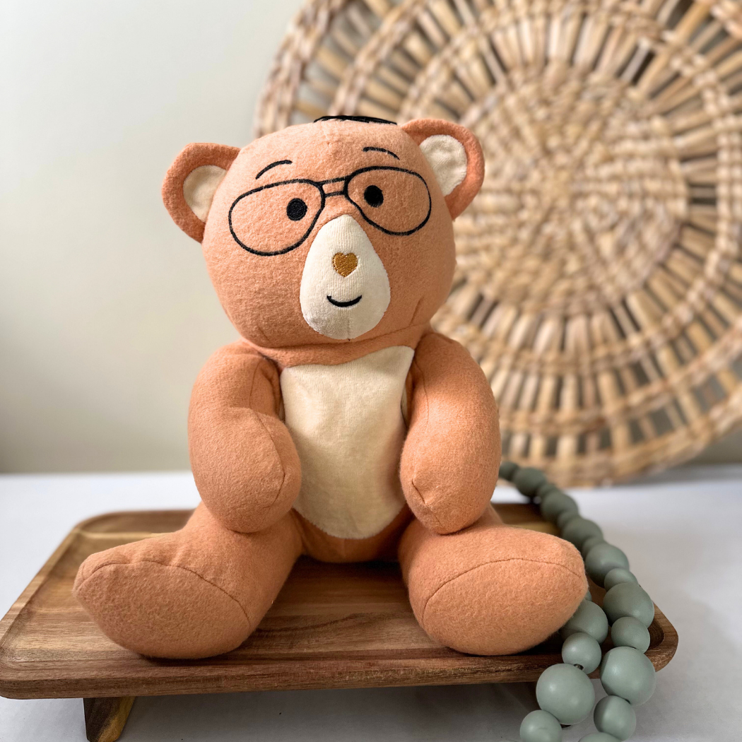 Plush teddy bear with glasses on a wooden tray with a woven basket in the background