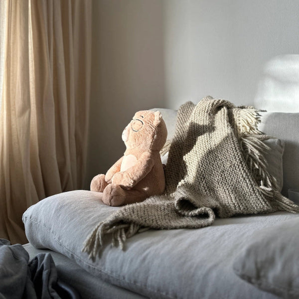 Percy bear and knitted blanket on a sofa with a curtain in the background