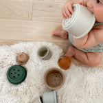 Baby sitting on floor chewing on stacking cup