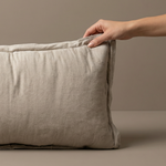 Beige pillow on a beige background with a hand touching it