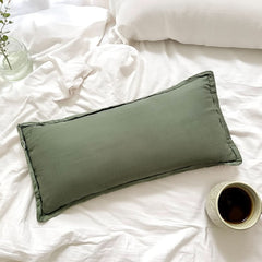 Green pillow on a white bed with a cup of coffee and a plant.