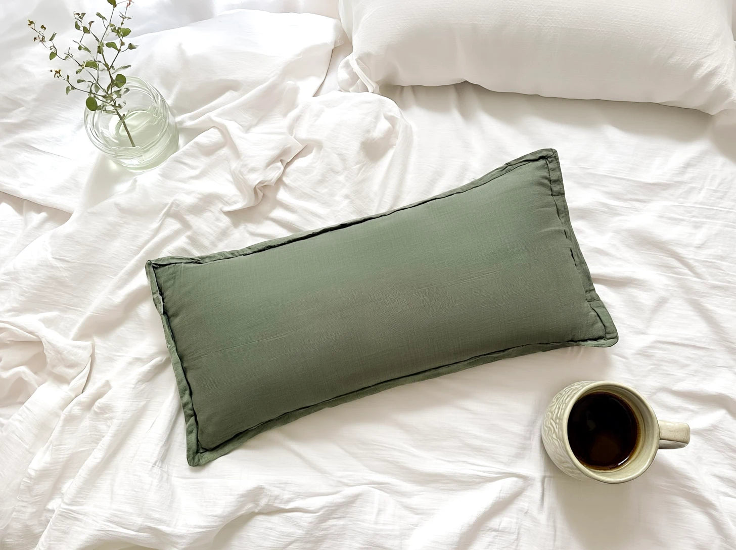 Green pillow on a white bed with a cup of coffee and a small plant.