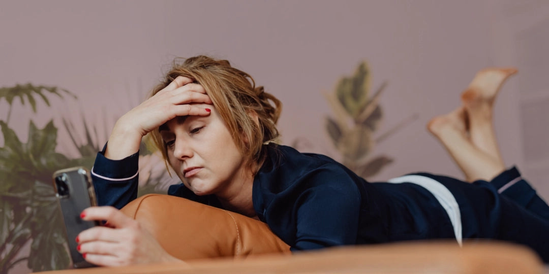 Woman lying on a couch using a smartphone with a neutral background unable to rest