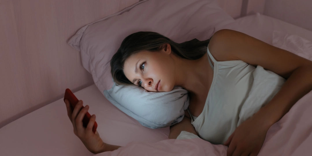 Woman lying in bed using a smartphone in a dimly lit room hav ing trouble sleeping