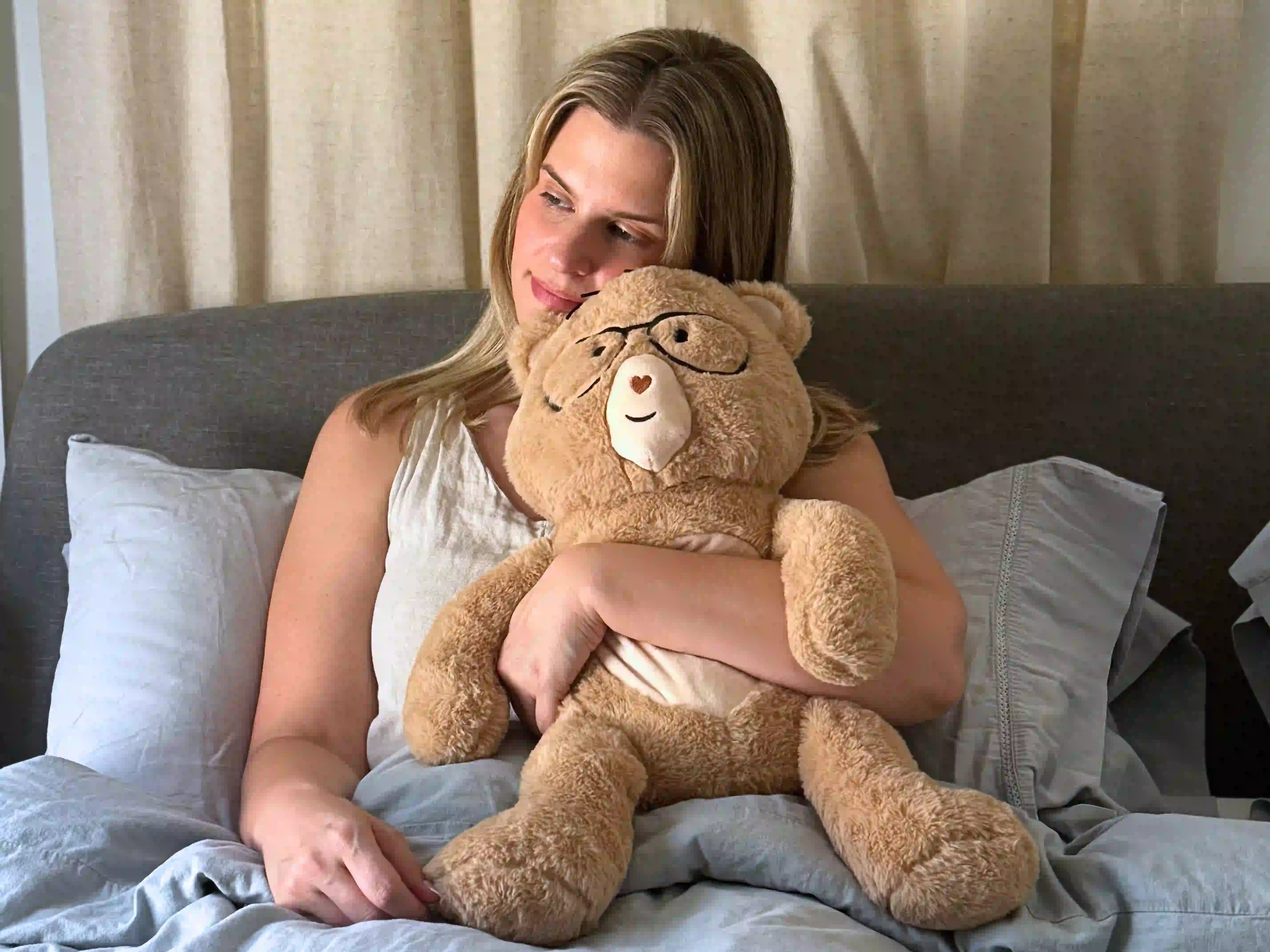 Woman holding  Percy bear with glasses on a bed