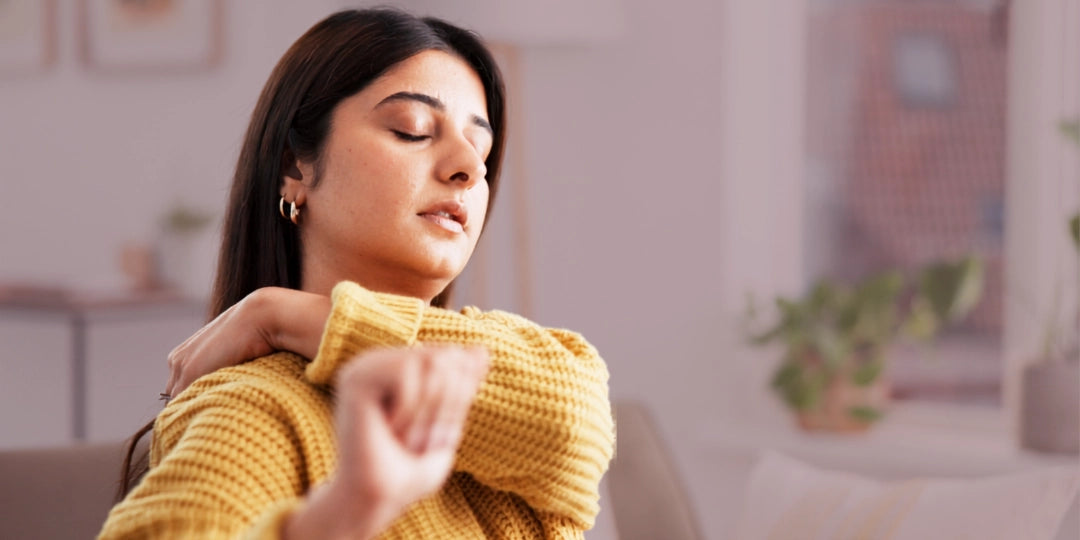 Woman in a yellow sweater sitting on a couch with a blurred indoor background with sore trap muscles